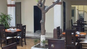 Un'area pranzo con tavoli e sedie, un albero in vaso e una scala che conduce a un piano superiore.