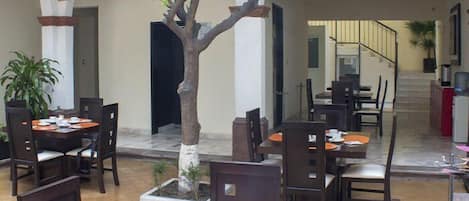 A dining area with tables and chairs, a potted tree, and a staircase leading to an upper level.