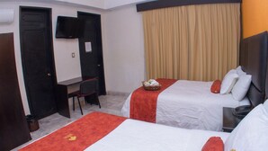 Una camera d'albergo con due letti, una scrivania, una sedia e un televisore appeso al muro.