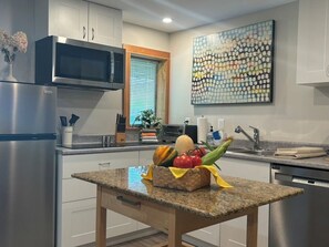 A modern kitchen with stainless steel appliances, a granite countertop, and a decorative fruit basket.
