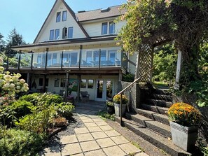 A two-story house with a covered porch, a staircase, and a garden with various plants and flowers.