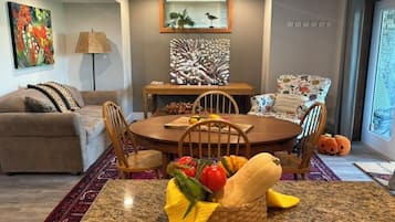 Un coin repas avec une table ronde, des chaises, un panier de fruits et une vue sur l’extérieur.