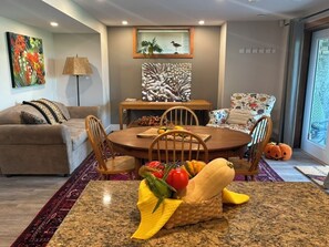 A dining area with a round table, chairs, a fruit basket, and a view of the outdoors.