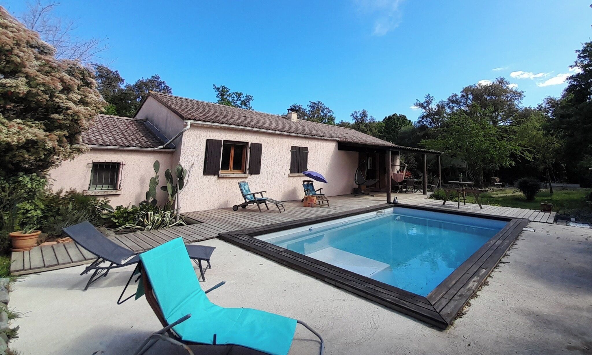 Una casa con piscina, un patio con sillones de descanso y un espacio al aire libre techado.