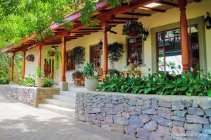 A covered porch with stone steps, wooden columns, and potted plants. - El Guayacán (Masaya)