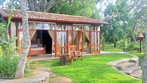 Una estructura de madera acogedora de un solo piso con ventanas amplias y un balcón, rodeada de abundante vegetación y un camino de piedra.