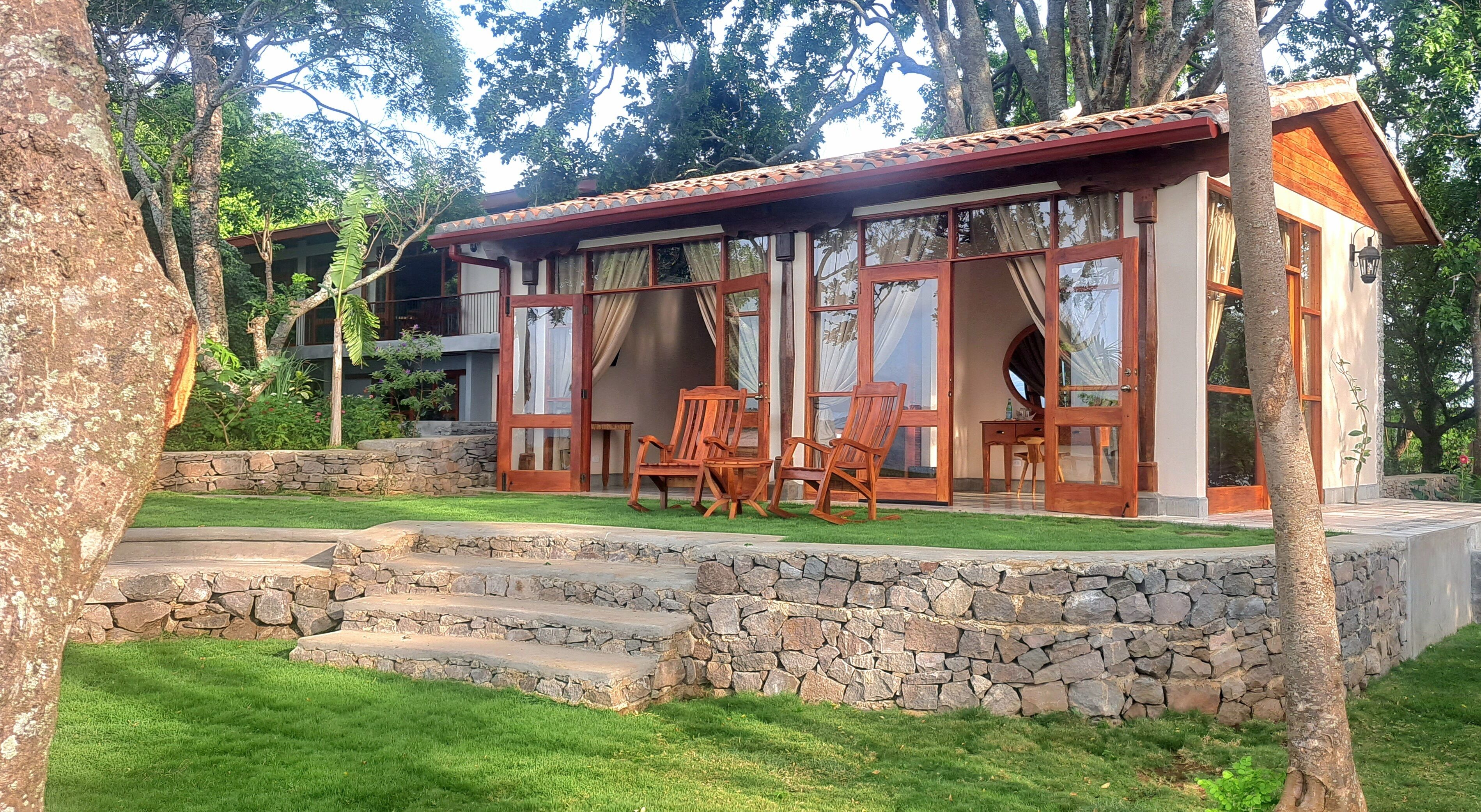 Una casa con una escalera de piedra que da a una terraza de madera, rodeada de abundante vegetación y árboles.