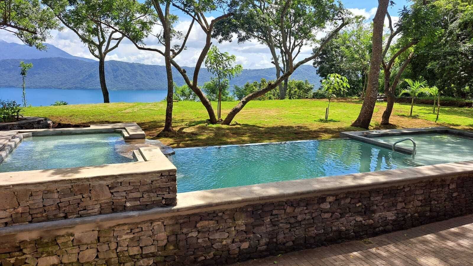 A swimming pool with stone walls, surrounded by trees and a view of mountains.