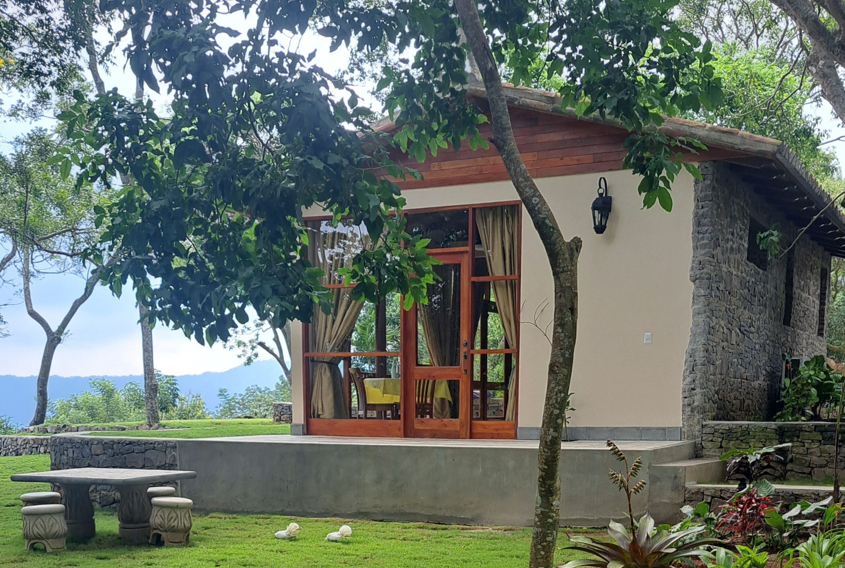 A rustic-style building with a stone exterior, large glass doors, and a small patio area with a table and chairs.