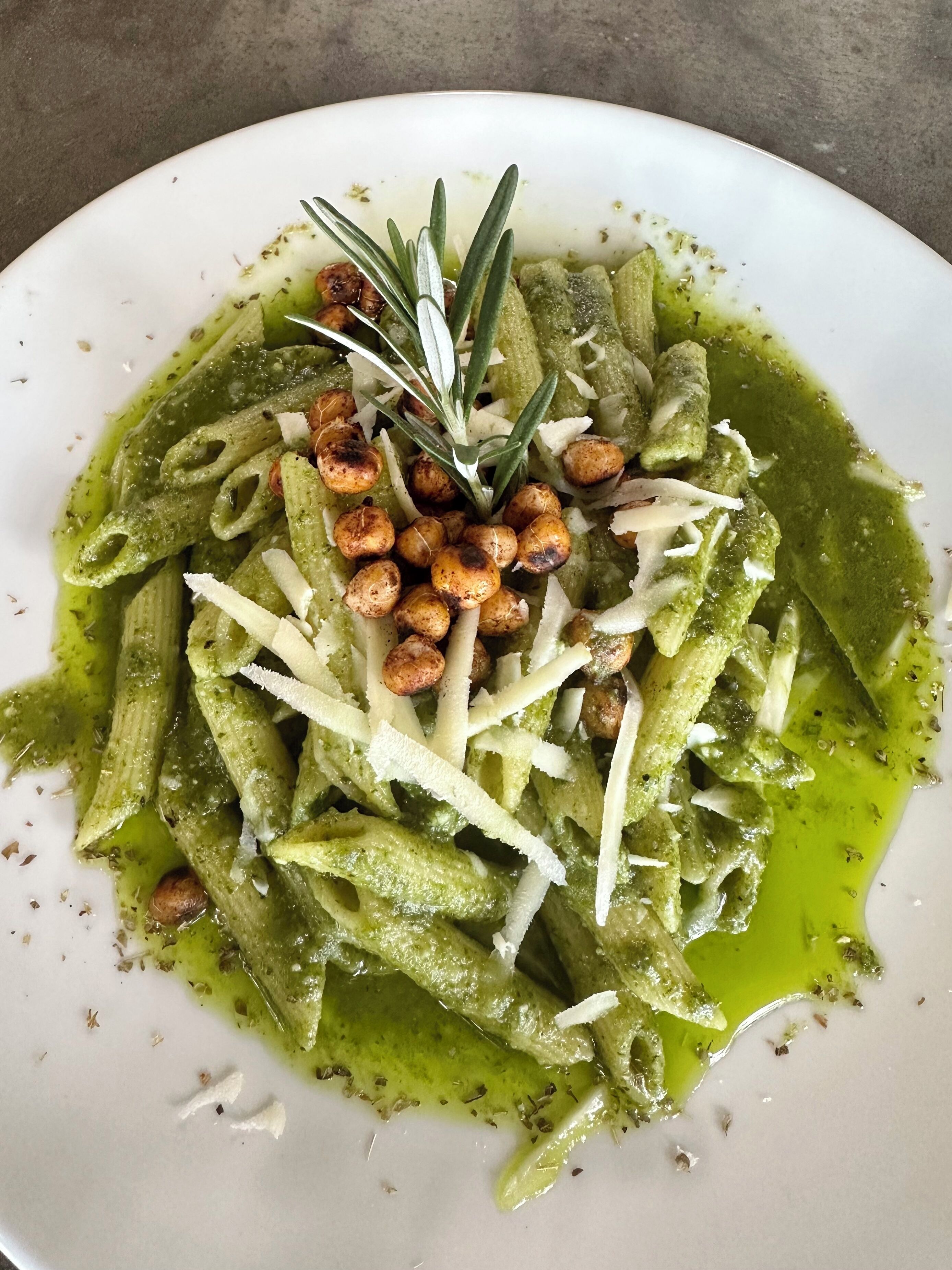 A plate of pasta with green sauce, garnished with herbs and nuts.