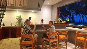 Zona de bar con sillas de madera, una barra y vista a árboles a través de una ventana.