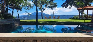 A pool area with a clear view of a mountain range, surrounded by trees and outdoor seating. - El Guayacán (Masaya)