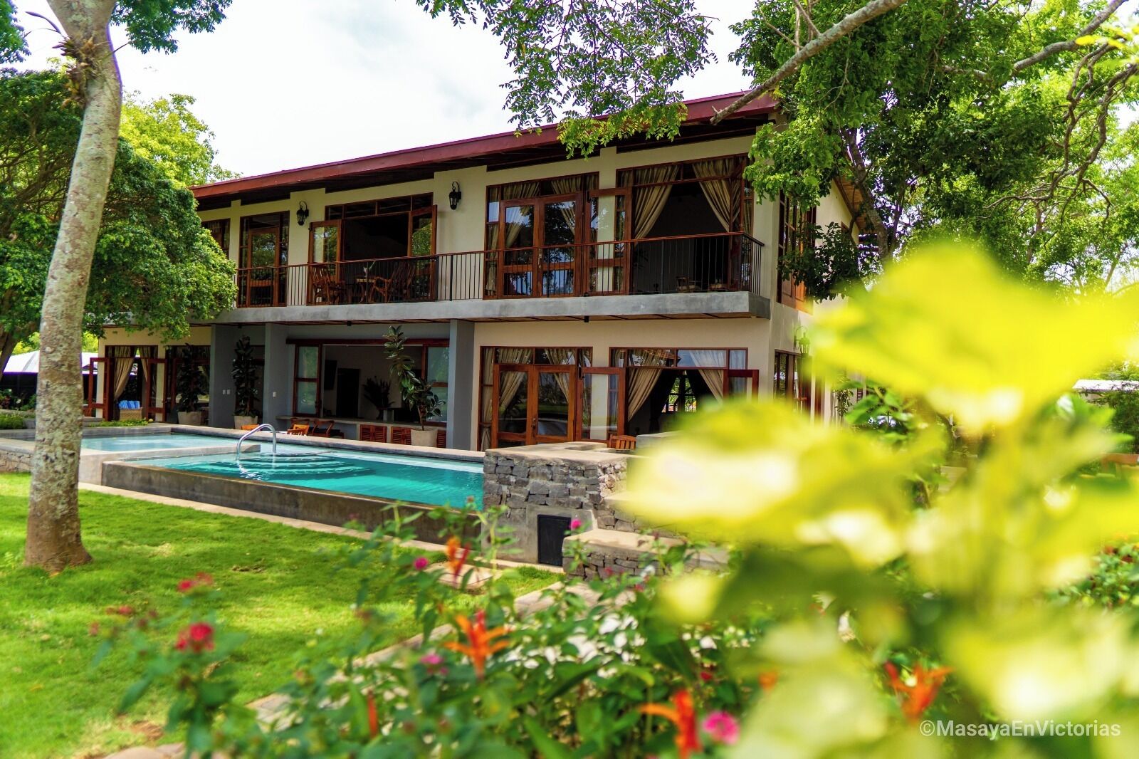 A two-story building with a swimming pool, surrounded by lush greenery and trees.