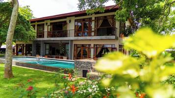 A two-story building with a swimming pool, surrounded by lush greenery and trees.