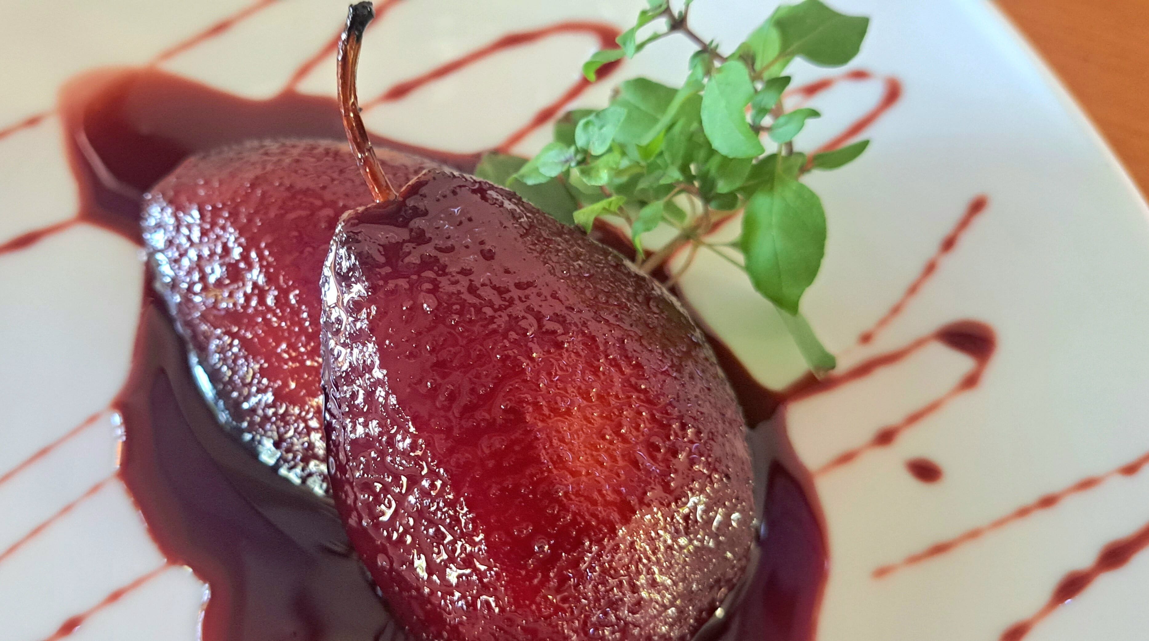 A pear with a glossy glaze and a sprig of greenery on a plate.