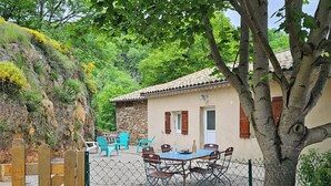 A rustic house with a stone wall, a wooden gate, and a fenced patio area with outdoor furniture. - Maison de Campagne au Coeur du Parc Naturel Regional des Monts D'ardeche (Issamoulenc)