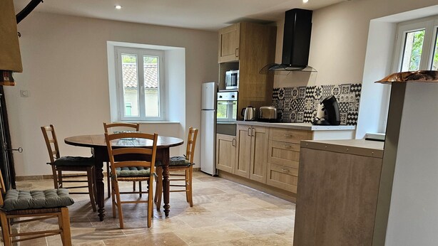 A modern kitchen with a dining area, featuring a central island, built-in appliances, and a patterned backsplash. - Maison de Campagne au Coeur du Parc Naturel Regional des Monts D'ardeche (Issamoulenc)