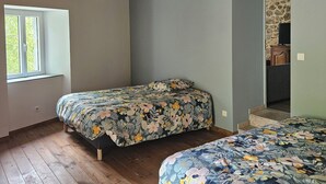 A bedroom with two beds, wooden ceiling beams, a window, and a stone wall. - Maison de Campagne au Coeur du Parc Naturel Regional des Monts D'ardeche (Issamoulenc)