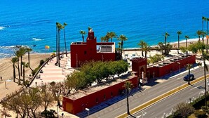 Une vue sur la côte, avec un bâtiment rouge, des palmiers et un ciel bleu dégagé.