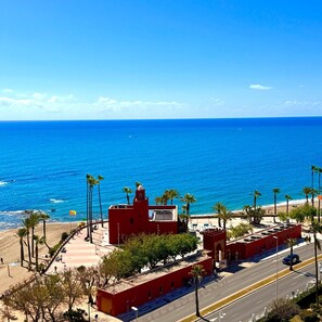 A coastal view with a red building, palm trees, and a clear blue sky.