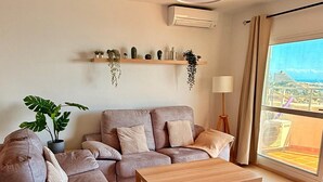 Un salon moderne avec un canapé d’angle, une table basse en bois et une grande fenêtre donnant sur la ville.