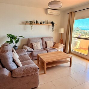 A modern living room with a sectional sofa, a wooden coffee table, and a large window with a city view.