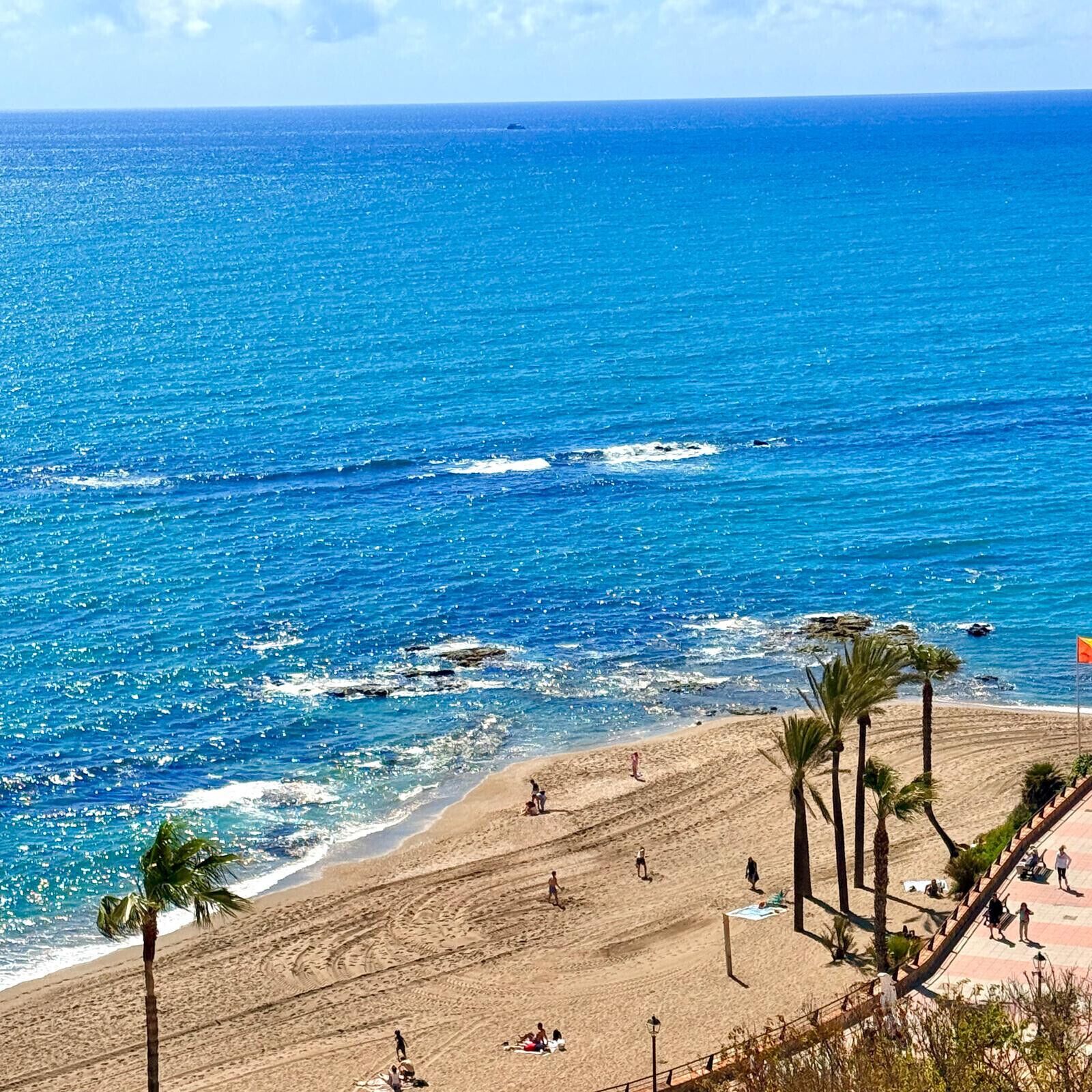A beach with clear blue water, palm trees, and people sunbathing.