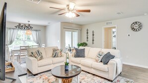 A living room with two sofas, a coffee table, a ceiling fan, and a large window. - Palm Coast Duplex w/ Screened Patio, Near Beaches! (Palm Coast)