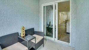 A balcony with wicker furniture and a glass table, leading to a room with a white door and a wooden floor. - Palm Coast Duplex w/ Screened Patio, Near Beaches! (Palm Coast)
