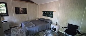 Un dormitorio con cama, mesitas de noche, una silla y un adorno en la pared.