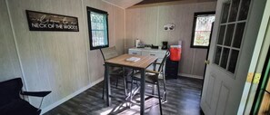 Una habitación con una mesa de madera, sillas, una pequeña zona de cocina con un refrigerador y una puerta con ventana.