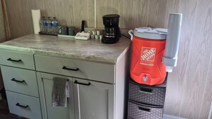 Una kitchenette con cafetera, botellas de agua y un dispensador de agua rojo.