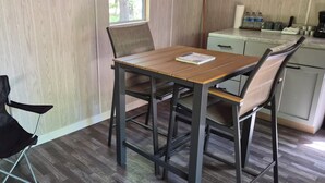 Una pequeña cocina americana con una mesa, sillas, un ventanal y un sillón con funda negra.