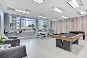 Un espacio recreativo moderno en el interior, con mesa de billar, asientos cómodos y amplias ventanas con vistas a la ciudad.