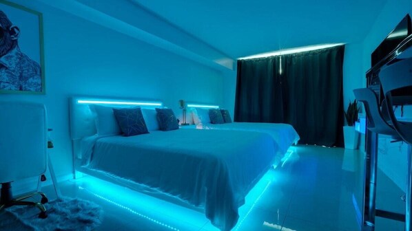 A modern hotel room with a large bed, bedside tables, a desk, and a flat-screen TV. - Modern Studio with Balcony, Pool, Gym & Games (Miami)