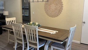 A dining area with a wooden table, white chairs, a decorative wall piece, and a modern pendant light. - Peaceful/Spacious Downtown home Branson near Lake Taneycomo w/great amenities   (Branson)