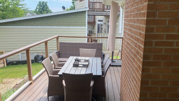 A covered outdoor patio with a wooden deck, wicker furniture, and a brick wall. - Peaceful/Spacious Downtown home Branson near Lake Taneycomo w/great amenities   (Branson)