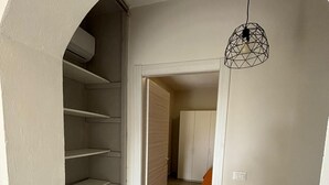 A hallway with a wooden staircase, a geometric pendant light, and a bed with an orange blanket in the background. - 3 Bedroom Apartment in Santa Maria (Santa Maria)