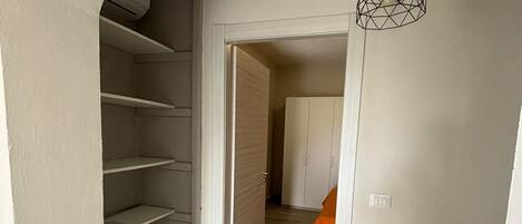 A hallway with a wooden staircase, a geometric pendant light, and a bed with an orange blanket in the background.