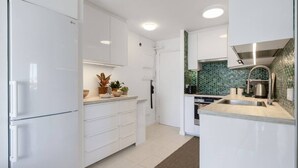 Una cocina moderna con armarios blancos, horno empotrado, pileta de acero inoxidable y un salpicadero de mosaico verde.