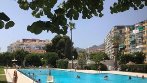 Una piscina con gente, rodeada de vegetación y edificios.
