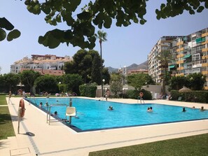 Una piscina con persone, circondata da vegetazione ed edifici.