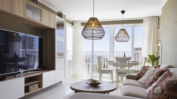 Una sala de estar moderna con un televisor de pantalla plana, un sofá, una mesa de centro y dos lámparas colgantes.
