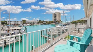 A marina with boats docked, a building in the background, and a balcony with turquoise chairs.