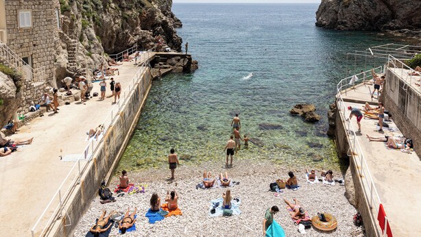 Eine Küstenlandschaft mit Felsen, klarem Wasser und Menschen, die sich sonnen und schwimmen.
