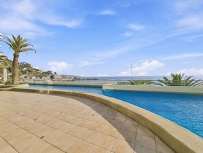 Une piscine à bord incurvé, entourée d’une terrasse carrelée.