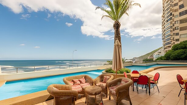 A poolside area with lounge chairs and a table, overlooking a beach and ocean. - Oceana Suites EuroVista (Vina del Mar)
