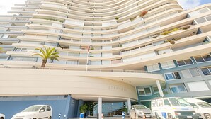 A multi-story hotel with a curved facade, balconies on each floor, and a parking area in front. - Oceana Suites EuroVista (Vina del Mar)