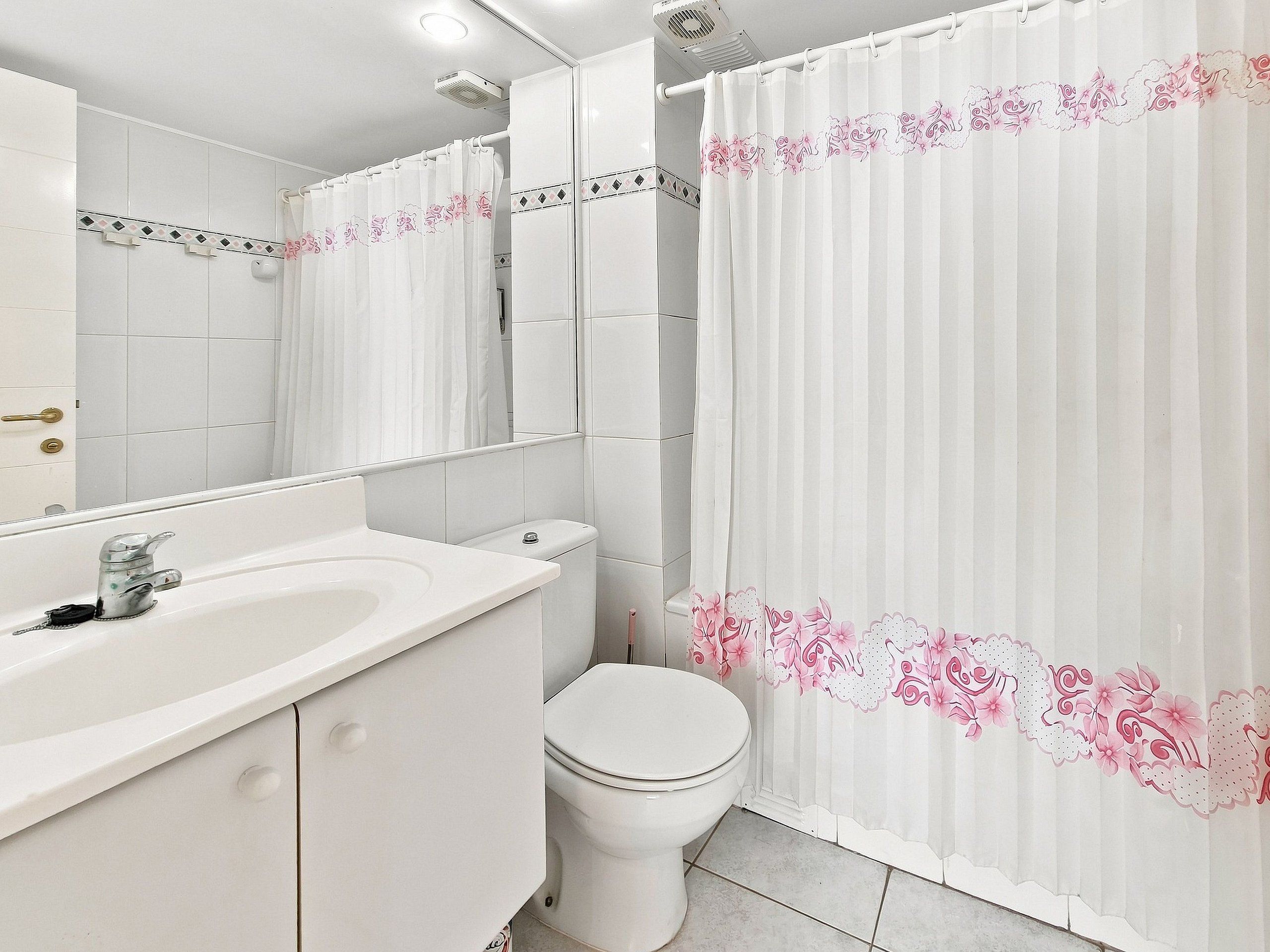 A bathroom with a white sink, toilet, and shower curtain with floral patterns.