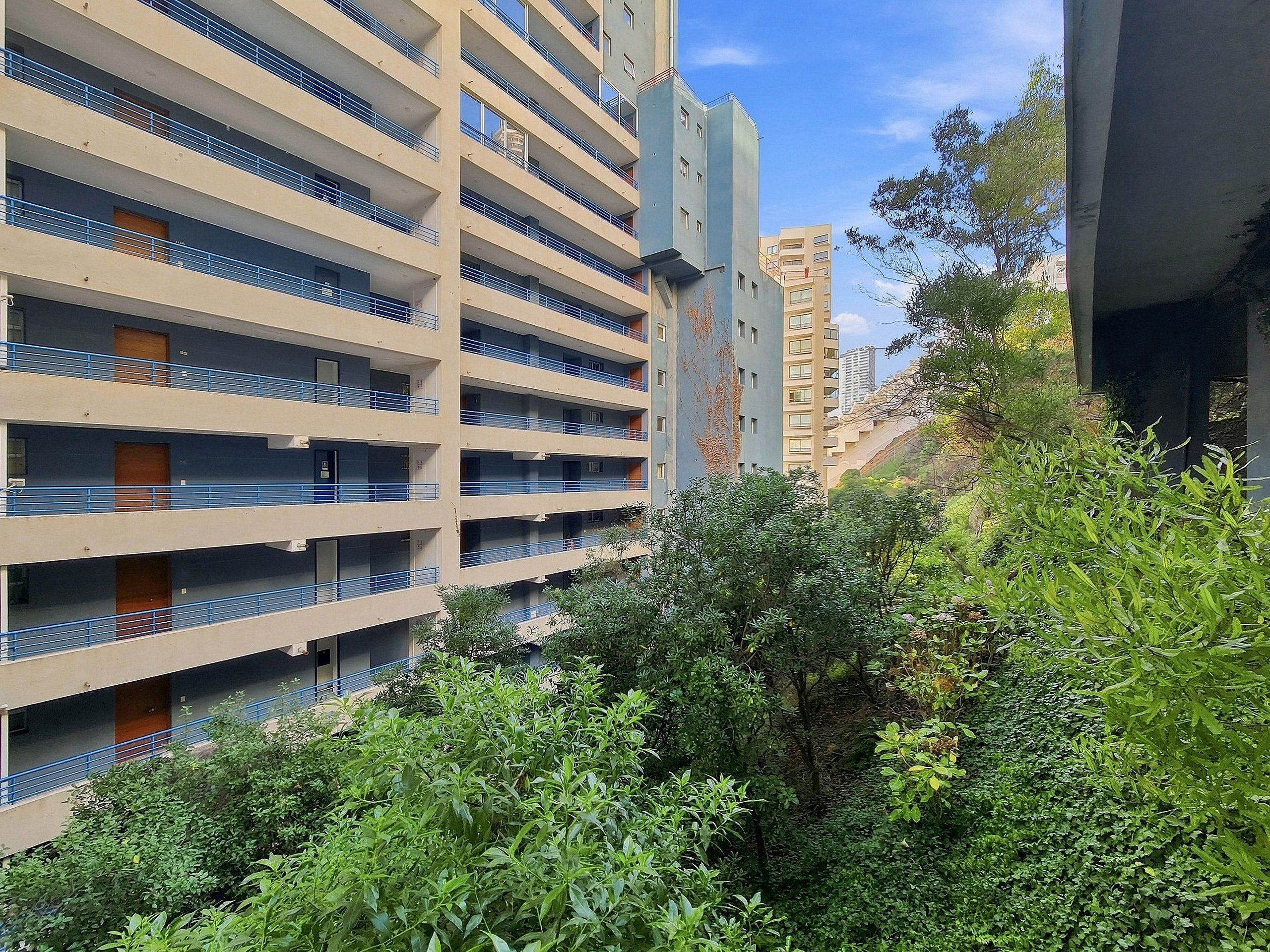 Un edificio de varios pisos con balcones, rodeado de vegetación.